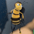 Pixelated yellow and black striped figure with large white eyes, dark limbs, and a rounded head against a gradient background.