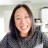 Pixelated static image of a person with long dark hair wearing a dark gray top against a light background with partial white text.