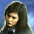 Pixelated image of a person with long dark hair wearing a dark hooded garment against a blue background.