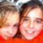 Two pixelated faces in close-up, one with light skin and brown hair on the left, another with lighter skin and dark hair on the right, both smiling against a red background.