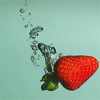 A red strawberry with green leaves and yellow seeds is partially submerged in water, with bubbles rising from its base against a light blue background.
