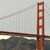 Pixelated static image of a red-orange suspension bridge tower with cables against a light gray sky and dark water below.
