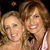 Two women with light brown hair smiling closely together against a dark background with a small blurred pinkish shape above.