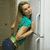 A woman in a teal shirt and dark pants leans against a white door frame with one arm, her head tilted back.