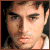 Pixelated close-up of a person's face with light skin tone, dark hair, and neutral expression against dark background.