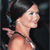 Pixelated profile view of a person with dark hair tied back, wearing a dark strap over one shoulder against a dark background.