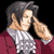 Pixelated image of a person with dark hair wearing a white checkered shirt under a maroon jacket, holding both hands near their face against a black background.