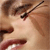 A pixelated close-up of a person's face with a dark object held near the mouth, set against a blurred background.