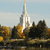 Pixelated static image of a tall white spire with a pointed top, surrounded by autumn-colored trees and a light blue sky.