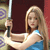 A pixelated figure with long blonde hair holds a sword, wearing a blue and white sleeveless top against a dark red background with patterned elements.