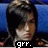 Pixelated image of a person with dark hair styled up, seated against blue background, wearing white top and black jacket, text 'grr.' at bottom.