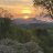 Pixelated sunset scene with warm orange and yellow sky transitioning to dark blue water, featuring a bright sun near the horizon and blurred landmass on the right.