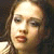 Pixelated close-up of a person's face with light brown hair, neutral expression, and visible eyes, nose, and mouth against a dark background.
