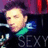 Pixelated image of a person with light skin and dark hair wearing a green shirt, holding a blue object near their face against a purple background.