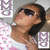 A person with dark hair and sunglasses wears a white top with pink patterns, positioned against a background with repeated 'M' symbols.