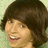 Pixelated close-up of a person with short dark brown hair, light skin, and a broad smile showing teeth, set against a pale green background.