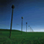 Static image of three tall dark poles on a green field under a blue sky gradient with no visible text or motion.