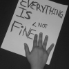 Black-and-white image of a hand holding a handwritten sign reading "EVERYTHING IS FINE" with "< NOT" written above "FINE".