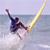 Pixelated static image of a person surfing on water with a yellow surfboard, viewed from an angle showing the board's side and the surfer's profile.