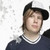 Pixelated static image of a person with light brown hair wearing a black cap and dark blue shirt with white collar trim against plain background.