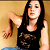 Pixelated image of a person with long dark hair wearing a black sleeveless top and blue pants, extending their right arm outward against a light brown background.