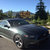 Pixelated static image of a dark vehicle on a road with blurred background elements including trees and buildings under a blue sky.