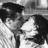 Black-and-white pixelated image of two figures in close proximity, one with dark hair and a light-colored shirt, the other with long dark hair, against a gradient background.