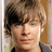 A pixelated portrait of a person with light brown hair and blue eyes, wearing a dark shirt with a gray collar, against a light background.