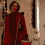 A person in a red coat with fur trim stands in a hallway with , transitioning from a raised arm pose to a relaxed stance