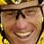 Pixelated close-up of a smiling person with light brown hair and glasses, wearing a yellow garment against a blurred background.