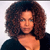 Pixelated portrait of a person with voluminous curly brown hair, wearing a dark top against a light background.