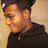 Pixelated close-up of a person wearing dark clothing and a cap, with visible ear and neck details against a light background.