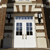 Static pixel art of a building facade with white double doors, blue-tinted windows, and brown architectural details.