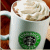 A white ceramic mug with a green circular logo, filled with brown liquid and topped with whipped cream, displayed in multiple views