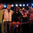 A split-screen image shows a group of people on stage with bright lights and a blue oval logo reading 'American Idol' on the right.