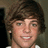 Pixelated image of a person with brown hair and green eyes, wearing white clothing against a dark background.