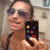 A pixelated image shows a person holding a black remote control with colored buttons, wearing sunglasses and a dark strap over the shoulder.