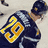 Pixelated image of a hockey player in dark uniform with yellow number 19 on back, standing against blue background with yellow text.