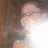 Pixelated static image of a person with light skin tone, dark hair, and a light-colored top with colorful accents, positioned against a brown background.