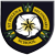 A circular badge with a dark blue background, yellow curved bands forming an outer ring, green foliage accents at top and bottom, and a central white circle containing a pixelated star-like symbol.