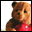 Brown bear with light tan face and red garment holds a pink sphere, head slightly turned left in first frame, then right in second frame.