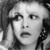 Black-and-white pixelated image of a person with light hair styled in waves, wearing a dark top, and holding a phone to their ear.