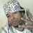 Pixelated image of a person wearing a silver helmet with white accents, holding an object near their face against a light background.