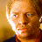 Pixelated static image of a person's face with warm lighting and orange-brown tones, likely from a movie or TV show character.