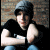 A pixelated image of a person in a black shirt and gray beanie leaning against a brick wall, with blue text reading "where is your boy tonight?" on the right side.