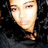 Pixelated close-up of a person's face with light skin tone, dark hair visible on the right side, and neutral expression against dark background.