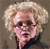Pixelated static image of a person with curly blonde hair, dark sunglasses, and pink lips against a brown background.
