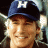 Pixelated image of a person wearing a dark blue cap with white 'H' logo, smiling against green background with bright green text.