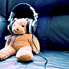 A pixelated brown teddy bear wearing silver headphones sits on a blue surface with a dark blue background.