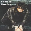 A person in a black leather jacket and dark shirt leans forward with hands clasped, set against a dark background with text reading 'They're Coming...' in the upper left.